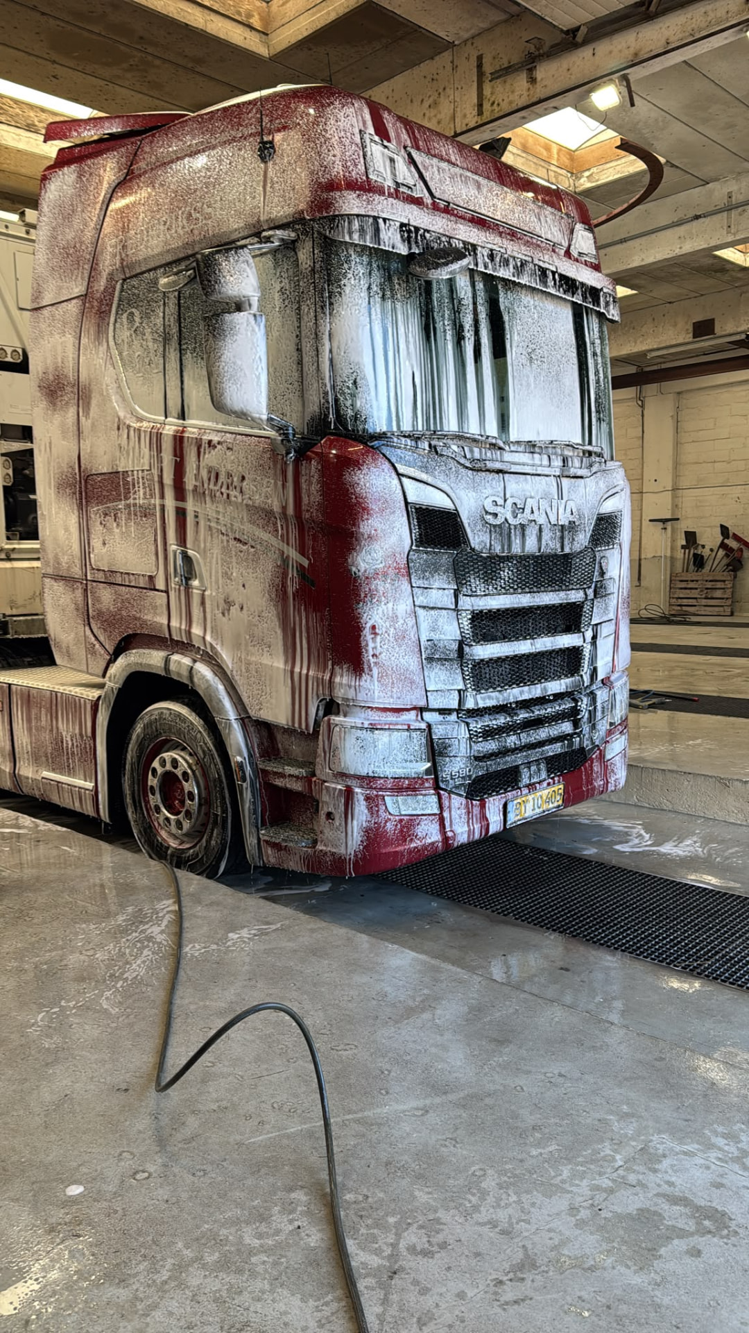Rød Scania-lastbil dækket af vaskeskum i vaskehal